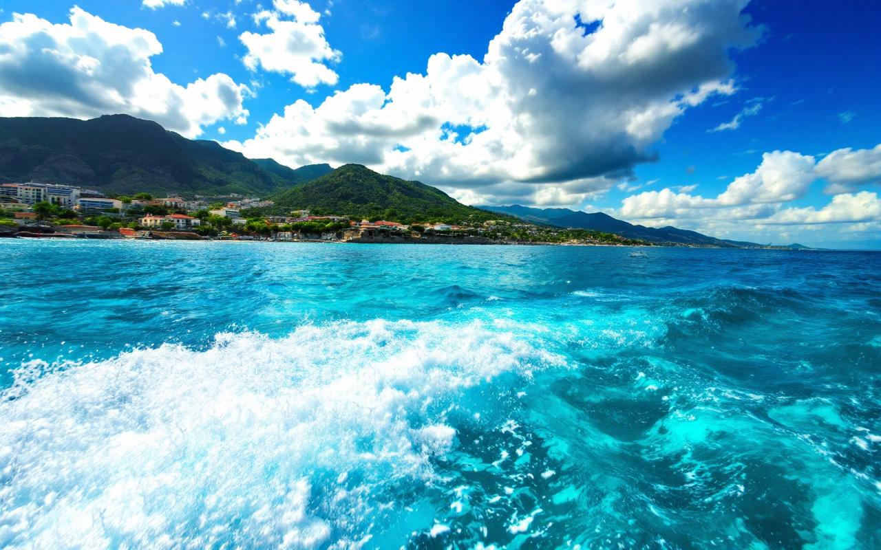 Un bateau naviguant sur la mer Méditerranée dans des eaux d'un bleu éclatant, sous un ciel ensoleillé, avec des vagues douces et une côte pittoresque en arrière-plan.