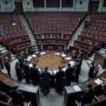 Quel gouvernement d’union nationale choisir après une crise politique ? Illustration réaliste d’un hémicycle parlementaire sous tension, avec des silhouettes de responsables autour d’une table de négociation, ambiance sobre et éclairage doux.