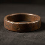 Bague antique en fer météoritique posée sur un tissu de musée sombre, éclairée latéralement pour révéler sa patine brune.