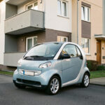 Petite voiture électrique citadine garée devant un immeuble résidentiel moderne, illustrant une solution de mobilité urbaine accessible avec un budget mensuel réduit.