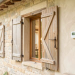 Maison ancienne lumineuse rénovée avec isolation naturelle, volets extérieurs, thermostat mural simple et matériaux chaleureux comme la pierre, le bois et l’enduit à la chaux.